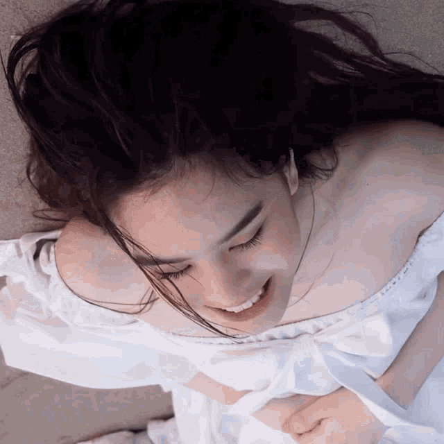 a woman in a white off the shoulder dress smiles with her eyes closed