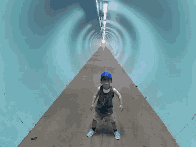 a young boy in a blue hat stands in a blue tunnel