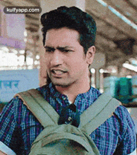 a man wearing a plaid shirt and a backpack is making a funny face .