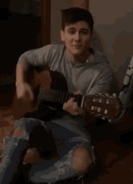 a young man is playing an acoustic guitar while sitting on the floor .
