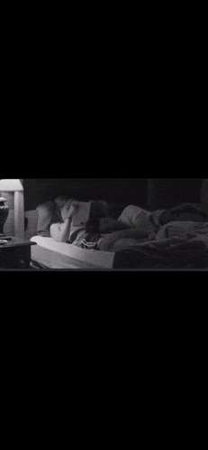 a person is laying on a bed reading a book in a black and white photo .