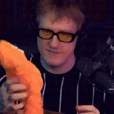 a man wearing glasses and headphones is holding a large piece of food in his hands .