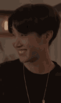 a young man wearing a black shirt and a necklace smiles