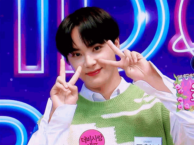 a young man wearing a green and white striped sweater giving a peace sign