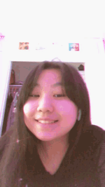 a girl with long dark hair is smiling in front of a pink background