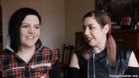two women are sitting next to each other in a room and smiling .