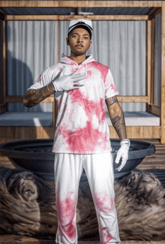 a man wearing a tie dye shirt and white gloves stands in front of a canopy bed