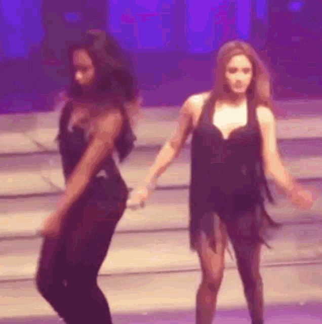 two women are dancing on a stage in front of a blue light .