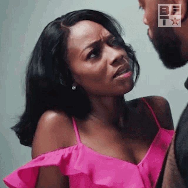 a woman in a pink dress is making a funny face while looking at a man in a suit .