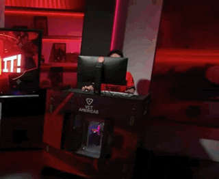 a man in a red shirt is sitting at a desk with a monitor and keyboard that says vct americas