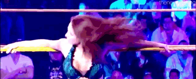 a woman is standing in a wrestling ring with her arms outstretched and her hair blowing in the wind .
