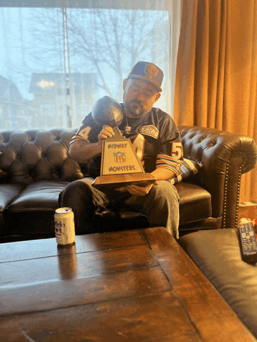 a man sitting on a couch holding a trophy that says midway nfl monsters