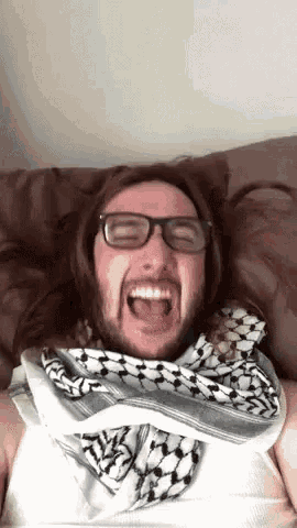 a man wearing glasses and a scarf is laying on a bed .