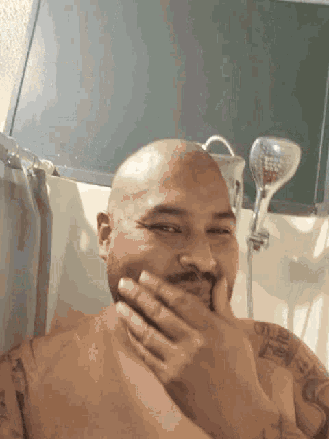 a shirtless man with a tattoo on his arm is laughing in a bathtub