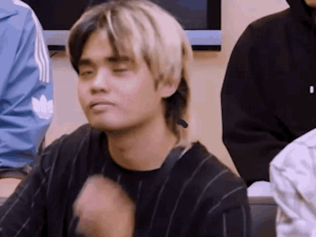 a young man with blonde hair is sitting in front of a group of people .