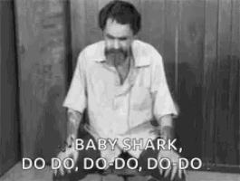 a man with a beard is kneeling down in a chair and singing baby shark .