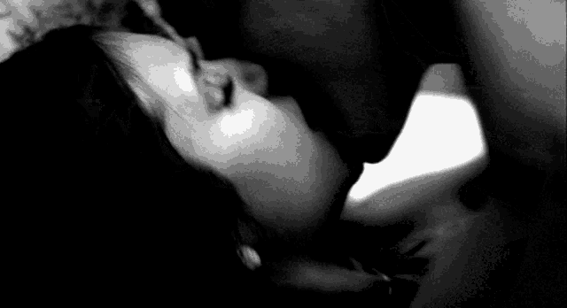 a black and white photo of a man and a woman kissing .