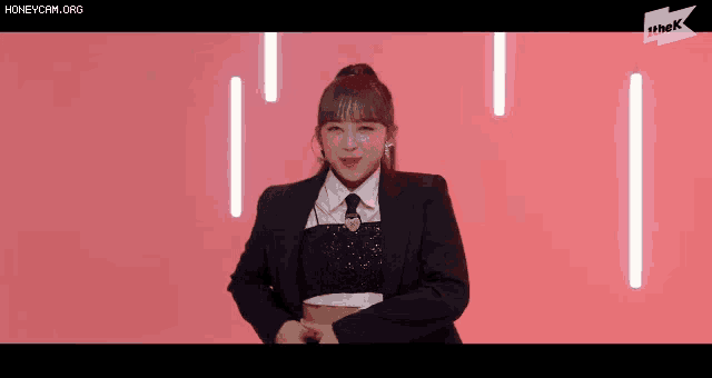 a girl in a suit and tie is dancing on a pink background .