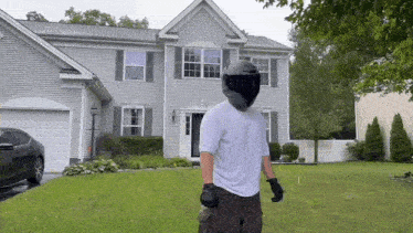 a man in a helmet and gloves is standing in front of a house .