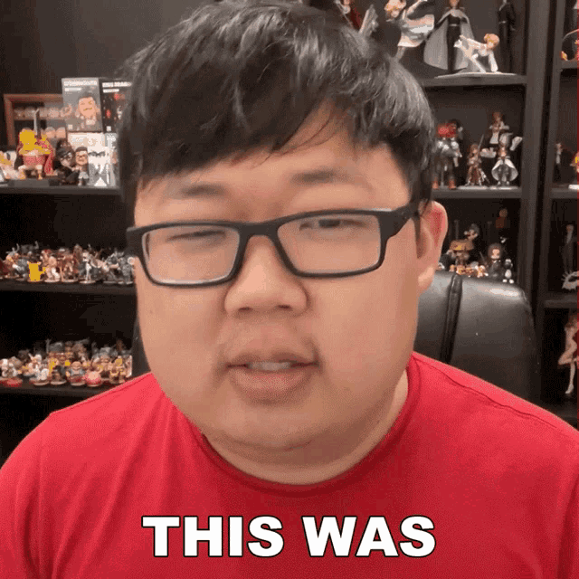 a man wearing glasses and a red shirt says " this was " in front of a shelf full of action figures