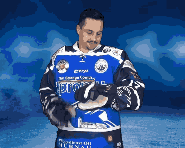 a man wearing a blue and white ccm jersey holds a hockey stick