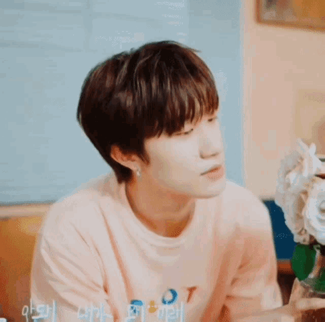 a young man wearing a pink shirt is sitting in front of a vase of flowers .