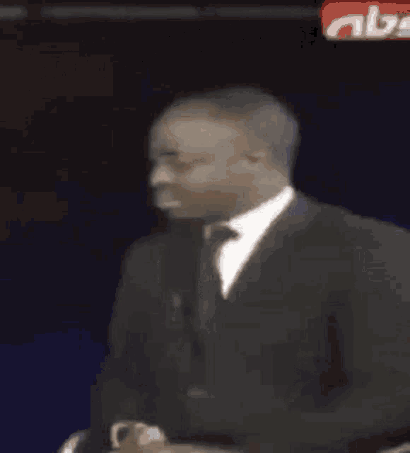 a man in a suit and tie is sitting in front of a screen that says `` why are you gay '' .