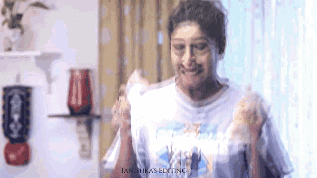 a woman wearing a white t-shirt with a picture of a beach on it is standing in front of a window ..