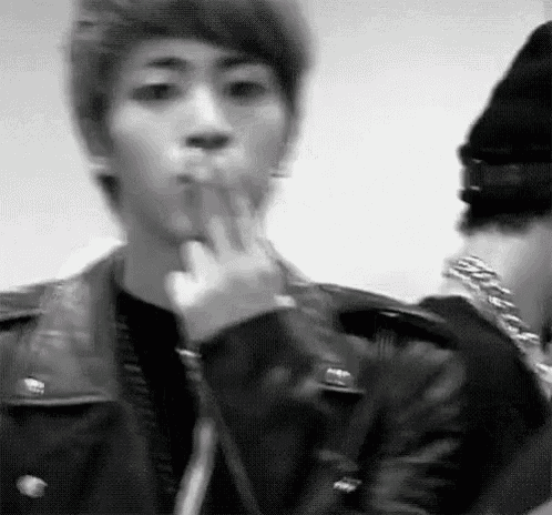 a black and white photo of a young man in a leather jacket smoking a cigarette .
