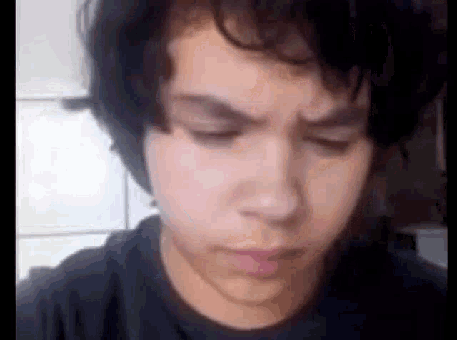 a close up of a young man 's face with his eyes closed and a black shirt on .