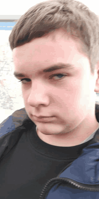 a young man with a black shirt and a blue jacket looks at the camera