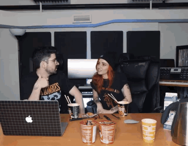 a man and a woman are sitting at a table with a laptop and cups of food