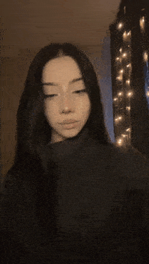 a girl with long dark hair is taking a selfie in front of a string of christmas lights