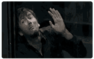 a man is screaming and covering his face with his hand while standing in front of a window .
