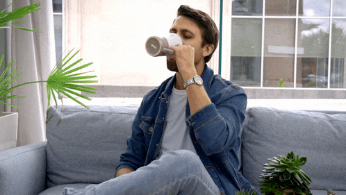 a man sitting on a couch drinking from a cup