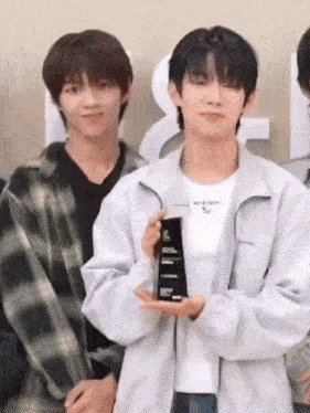 a young man is holding a trophy in his hand while standing next to another young man in a plaid shirt .