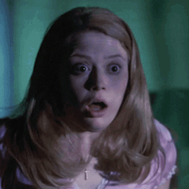 a woman in a pink shirt with a cross necklace is making a surprised face