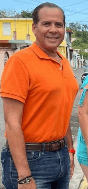 a man in an orange polo shirt and jeans is standing on a sidewalk .
