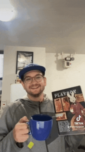 a man holding a playboy magazine and a blue mug