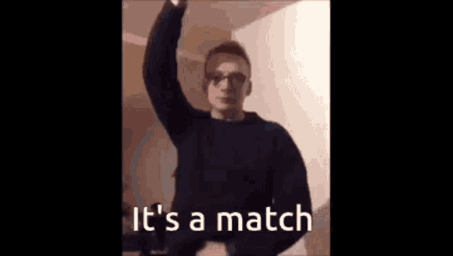 a man wearing headphones and a black sweater is standing in a room with his arm in the air .
