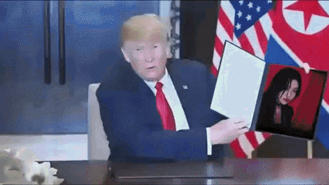 donald trump sitting at a desk holding a picture of a woman