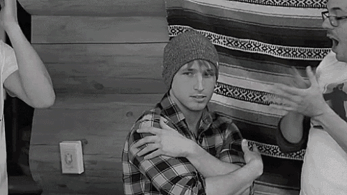 a man in a plaid shirt and a beanie is standing in front of a wall .