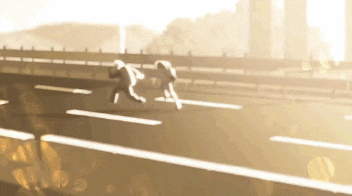 two people are running down a highway in the sunlight .