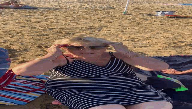 an older woman in a striped dress is laying on the beach
