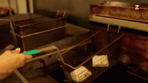 a person is holding a green tong over a fryer with the letter z in the corner