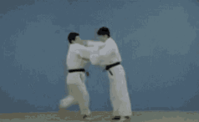 two men in white karate uniforms are fighting each other on a mat .