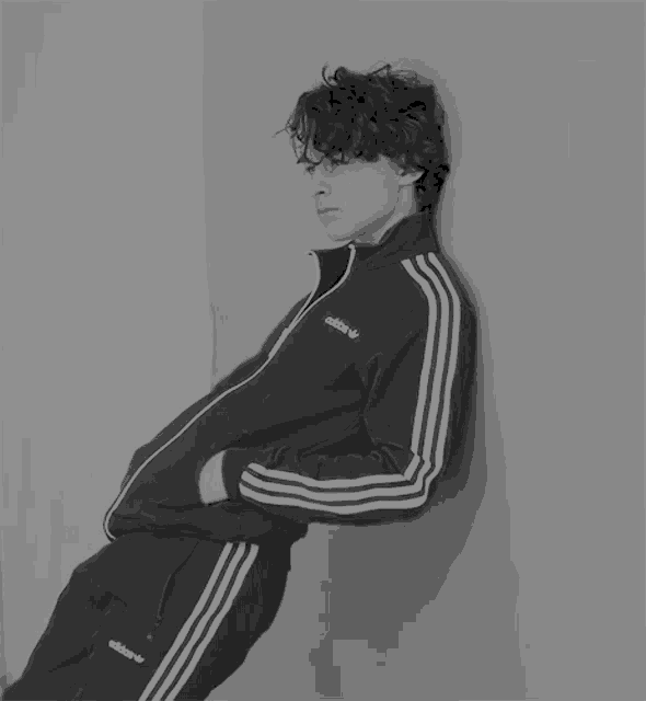 a young man leaning against a wall wearing an adidas tracksuit