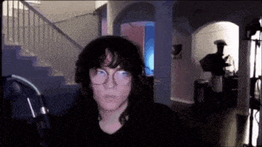 a woman wearing glasses and headphones is standing in front of a microphone in a dark room .