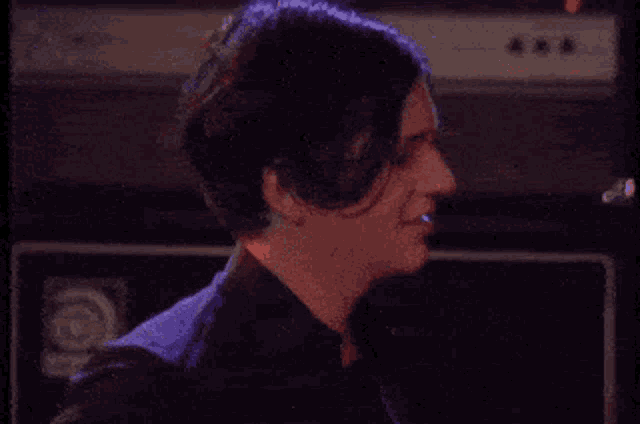 a man in a black shirt is smiling in front of an amplifier in a dark room .
