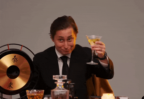 a man in a suit holds a martini glass in front of a gong with chinese characters on it